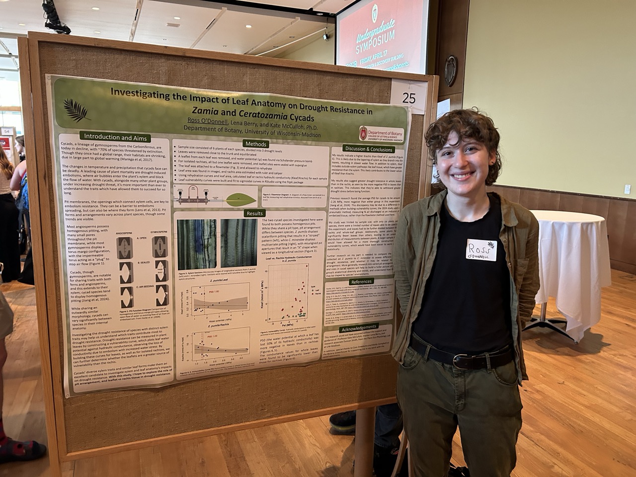 Ross stands in front of his research poster, smiling.